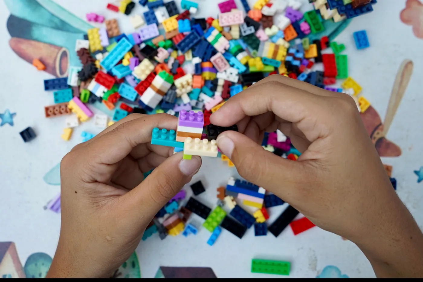 A child's hands pressing together colourful LEGO bricks above a loose pile of bricks on a table.